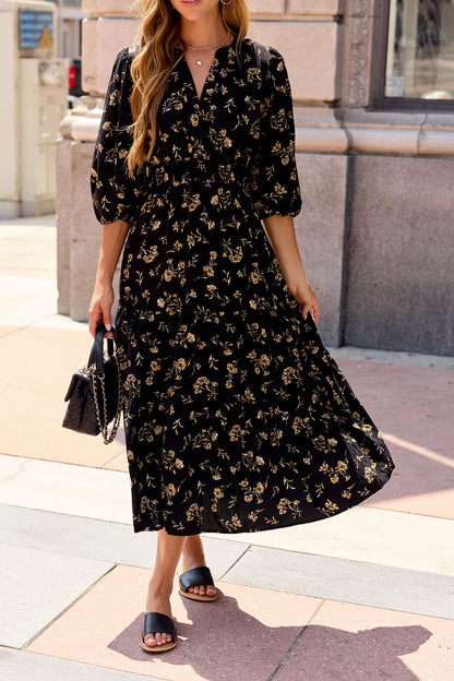 Woman in an Ember Floral Midi Dress - Black, holding a black bag and wearing black slide sandals.