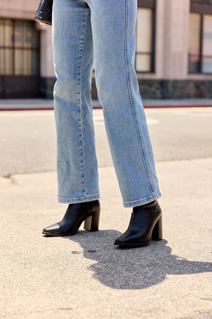 Person in light blue jeans and MIA Sidonie Leather Booties - Black | Pre Order, standing on a sunny city sidewalk.