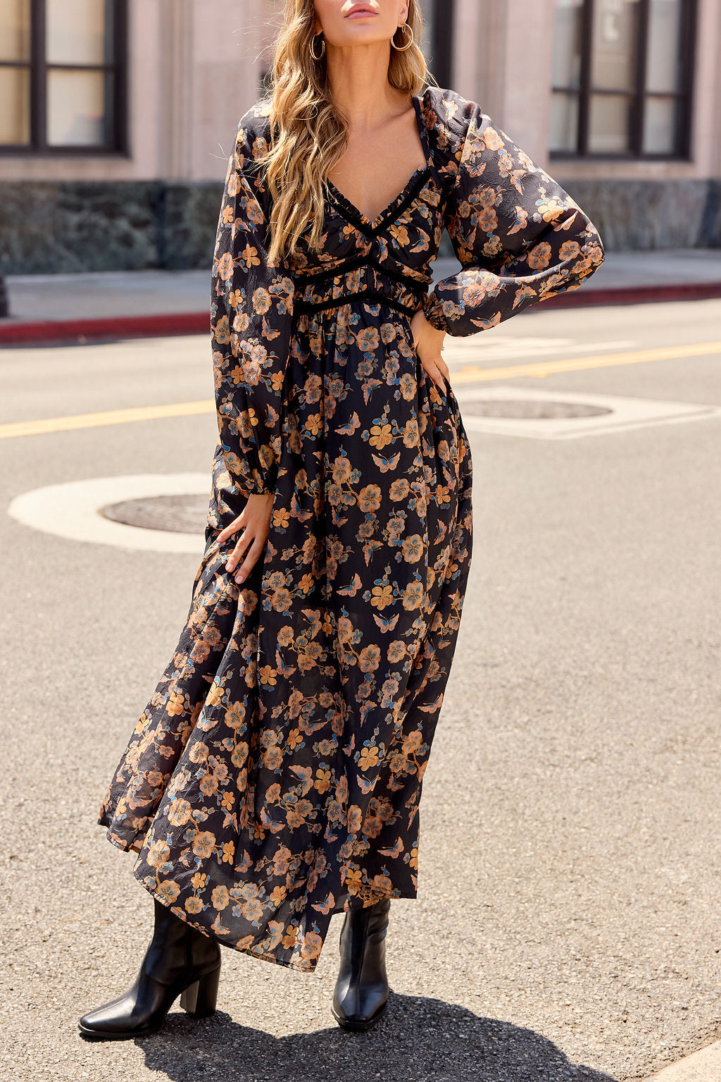 Woman wears the Maple Floral Maxi Dress - Black | Pre Order with boots, standing confidently on a city street, hand on her hip.