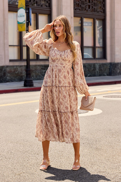 Woman in the Sweetheart Floral Print Midi Dress - Sand stands on a sunny street, holding a textured beige clutch.