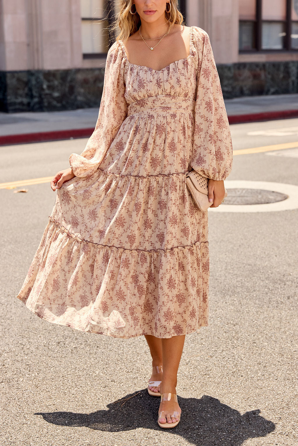 Woman wears Sweetheart Floral Print Midi Dress - Sand, holding her skirt and a woven clutch on a sunlit street.