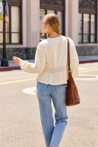 Woman in a Wren Textured Sweater - Cream and jeans, carrying a brown bag, walks on a sunny city street facing away.