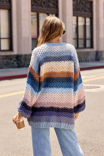 A person in a Multi Blue Stripe Crochet Cardigan holds a coffee cup on a city street, facing away from the camera.