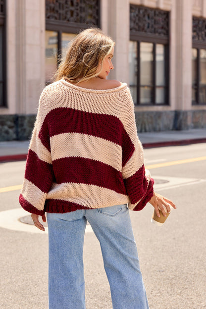 Woman in Camel & Wine Striped Sweater - Pre Order, wearing light blue jeans, stands on a city street with a coffee cup.