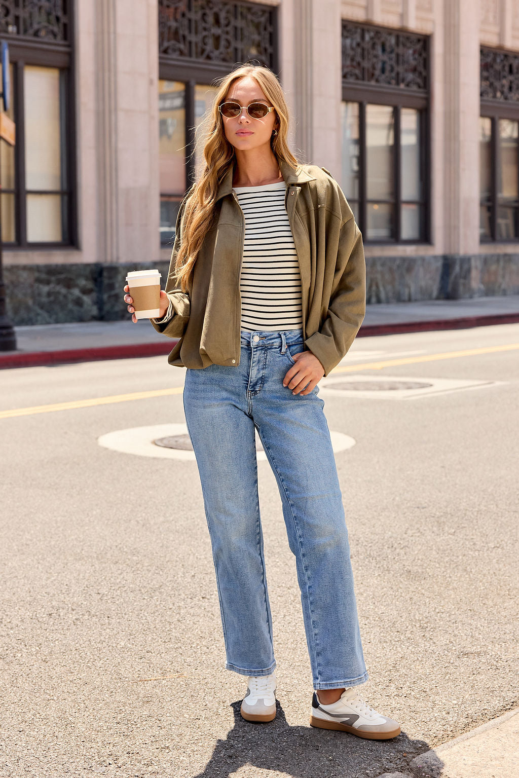 Woman in a striped shirt, jeans, and Suede Bubble Hem Jacket - Olive—cozy fall layering for strolling city streets with coffee in hand.