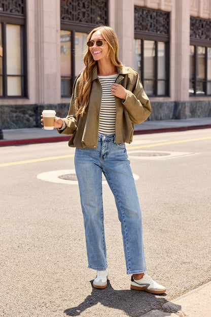 Woman in sunglasses with coffee, layering the Suede Bubble Hem Jacket - Olive over stripes and denim for chic fall city strolls.