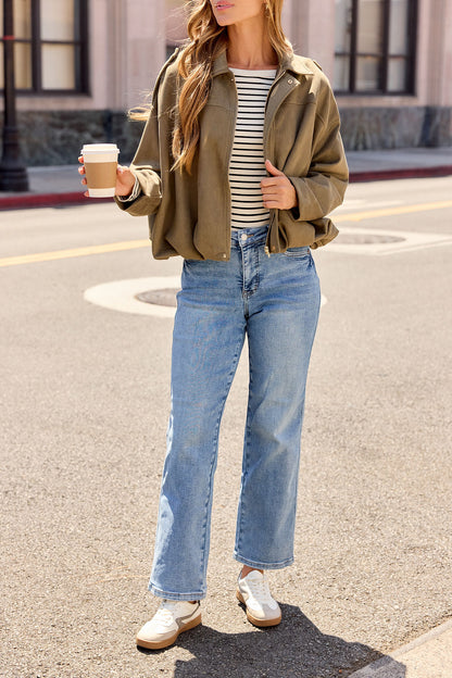 Woman in jeans and sneakers layers with the Suede Bubble Hem Jacket - Olive, holding coffee on a city street. Ideal for fall layering.