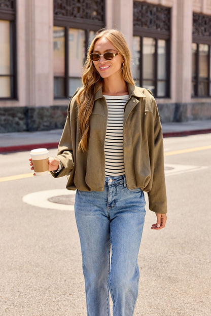 Woman in sunglasses, striped shirt, jeans, and the Suede Bubble Hem Jacket - Olive smiles with coffee on a city street.