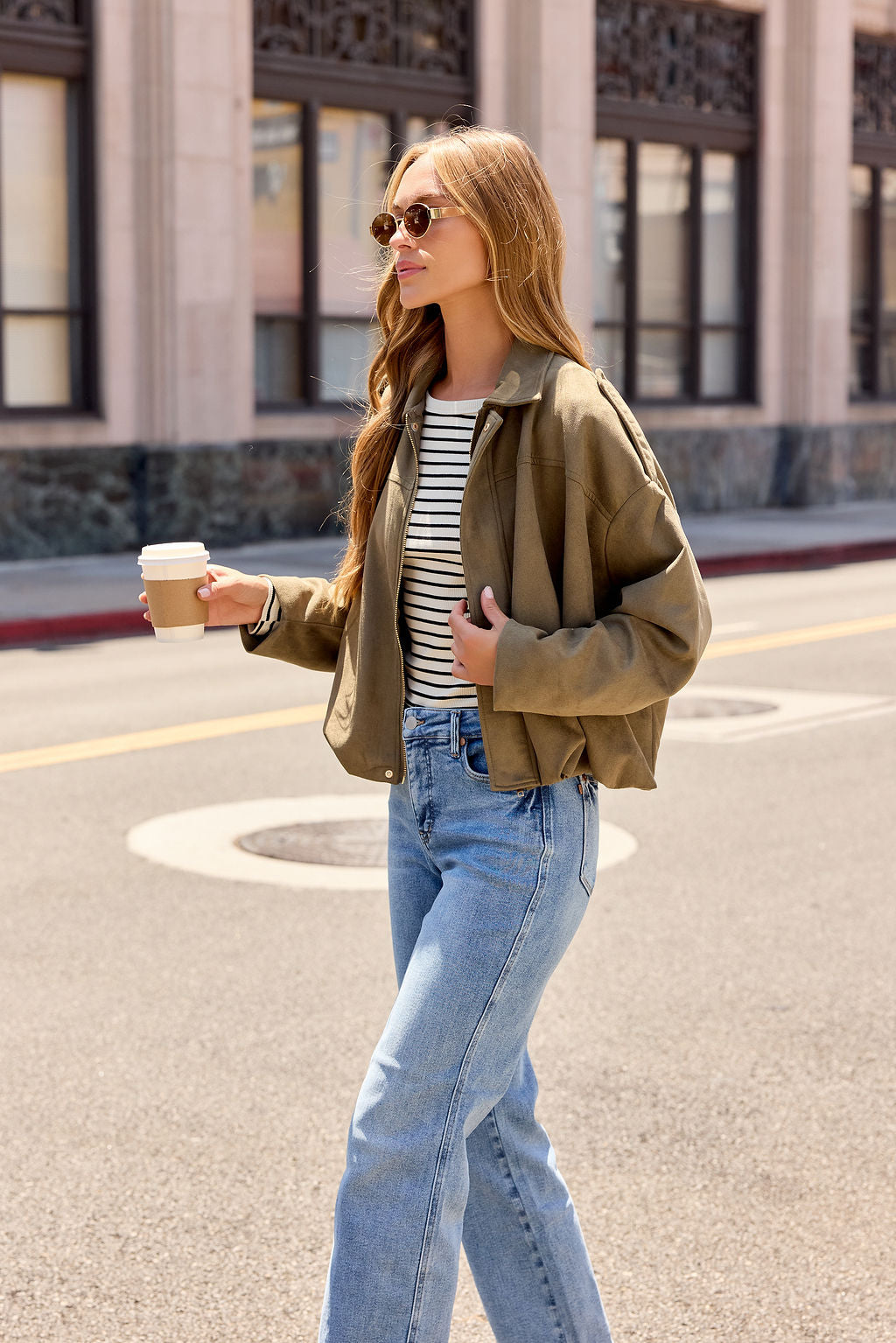 A woman in a striped shirt and Suede Bubble Hem Jacket - Olive nails effortless fall layering on a sunny day with coffee in hand.