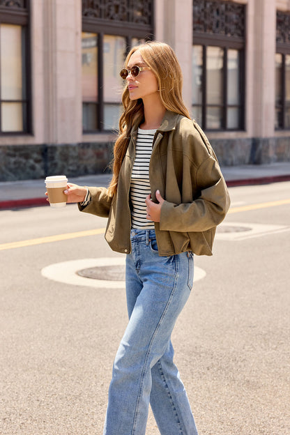 A woman in a striped shirt and Suede Bubble Hem Jacket - Olive nails effortless fall layering on a sunny day with coffee in hand.