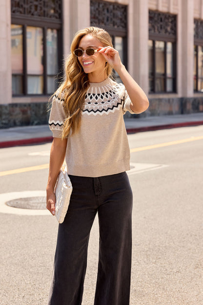 Woman in sunglasses wears a Taupe Aztec Print Sweater and wide-leg pants, smiling on a city street with a white clutch.