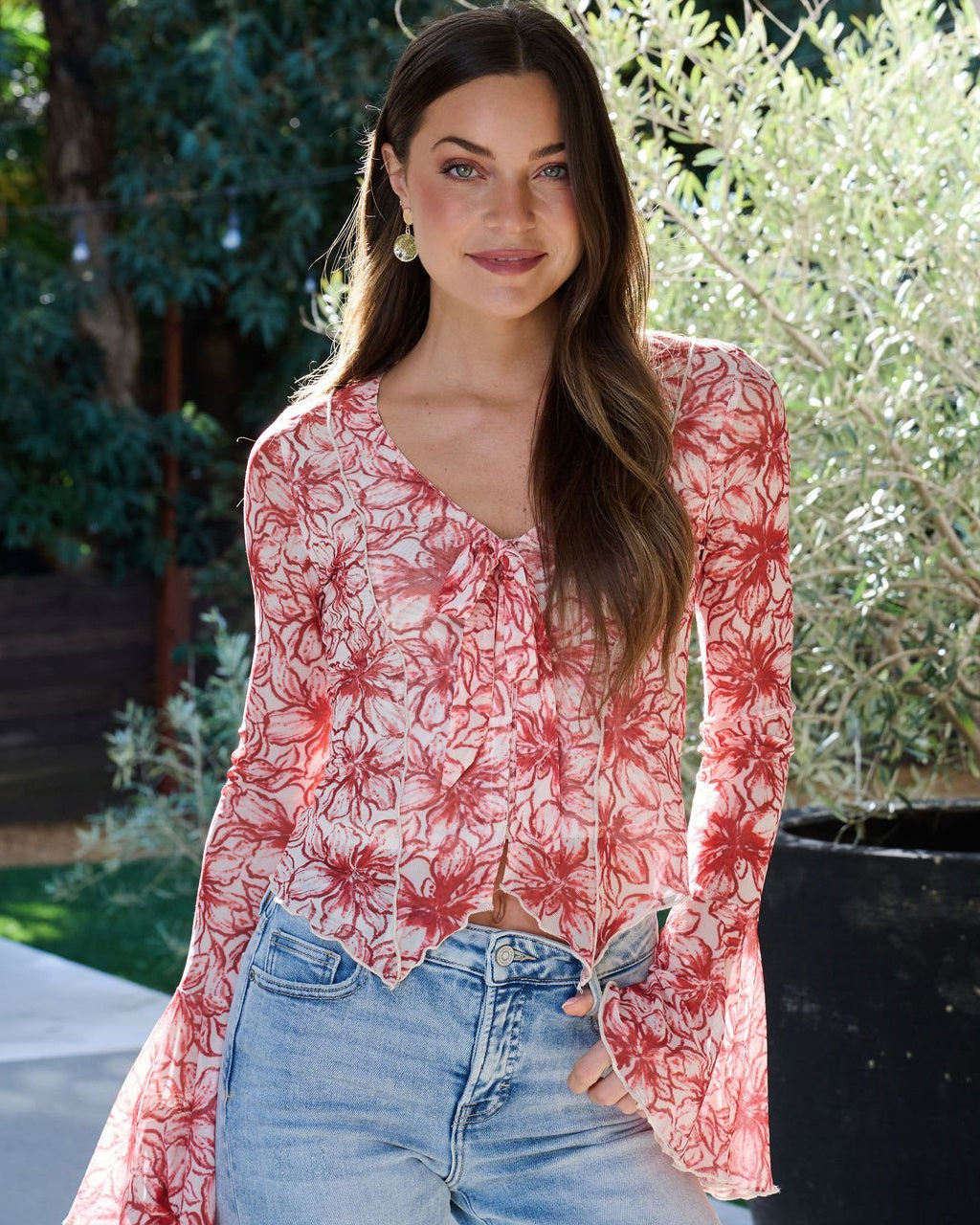 Woman wearing a red floral blouse and blue jeans outdoors.