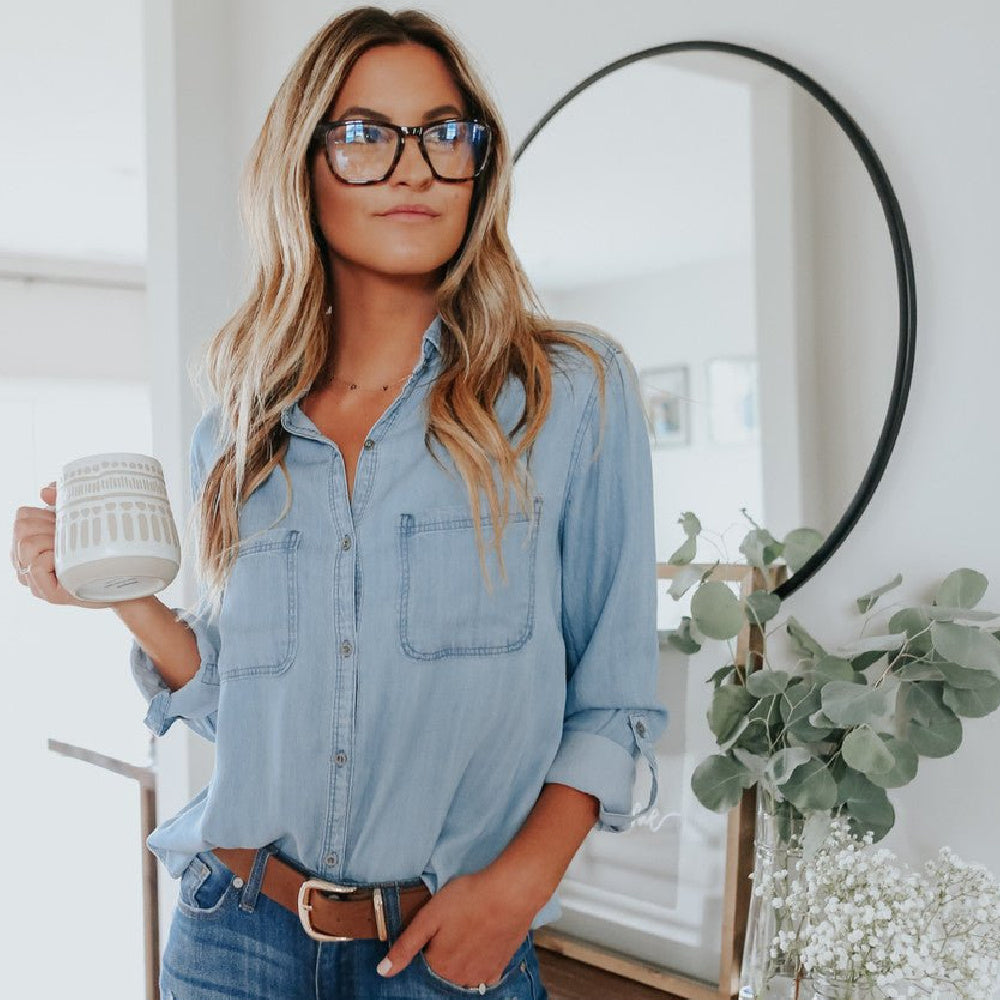 Woman wearing a denim shirt and holding a mug in a home setting