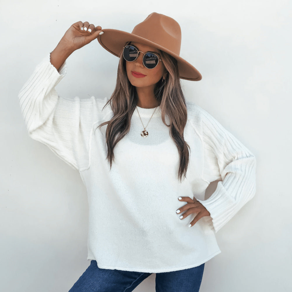 Woman wearing a white sweater, brown hat, and sunglasses on a plain background