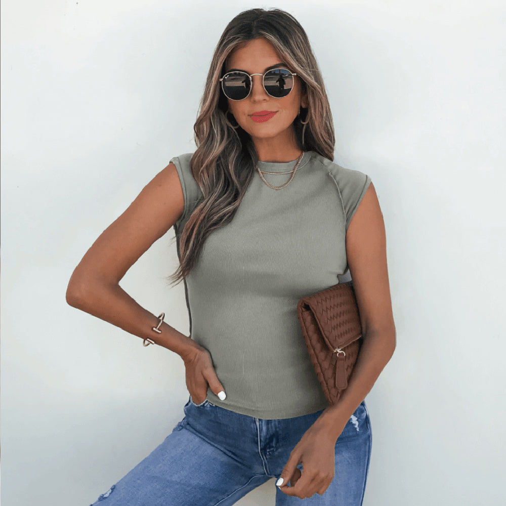 Woman wearing a green sleeveless top and blue jeans, holding a brown leather jacket against a white background.