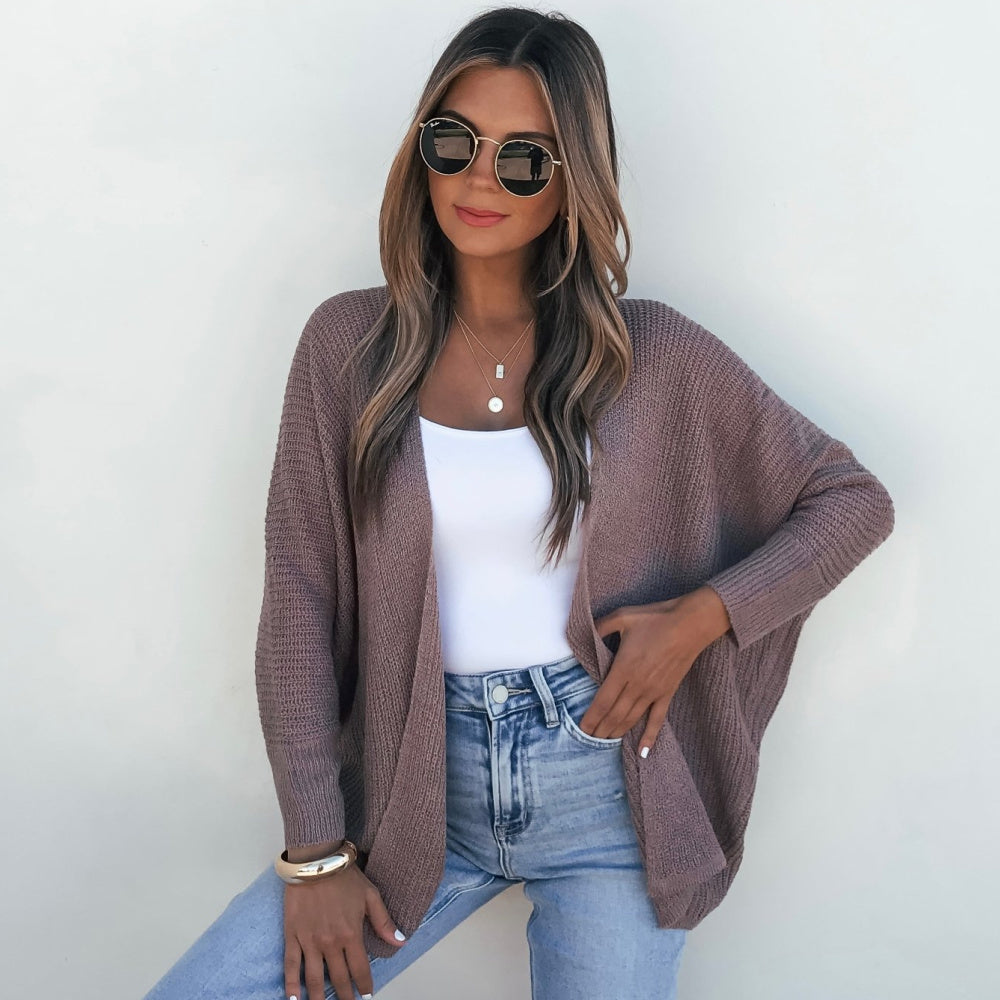 Woman wearing a brown cardigan, white top, and blue jeans against a white background