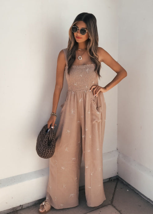 Woman wearing a beige jumpsuit with a plain white wall background