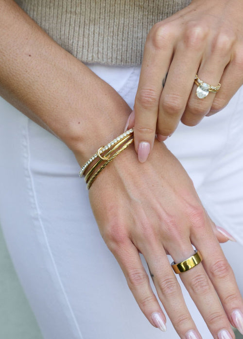 Close-up of hands wearing gold bracelets and rings on a white background