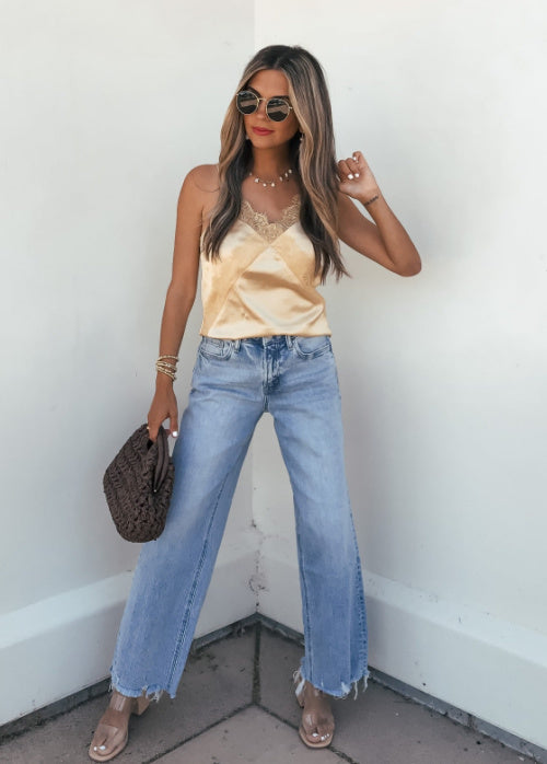 Woman wearing a yellow top and blue jeans against a white wall.