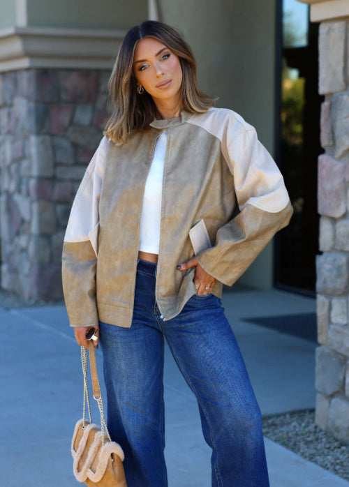 Woman wearing a patterned jacket and blue jeans standing in front of a stone building.