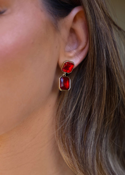 Close-up of a person wearing red gemstone earrings with gold accents.