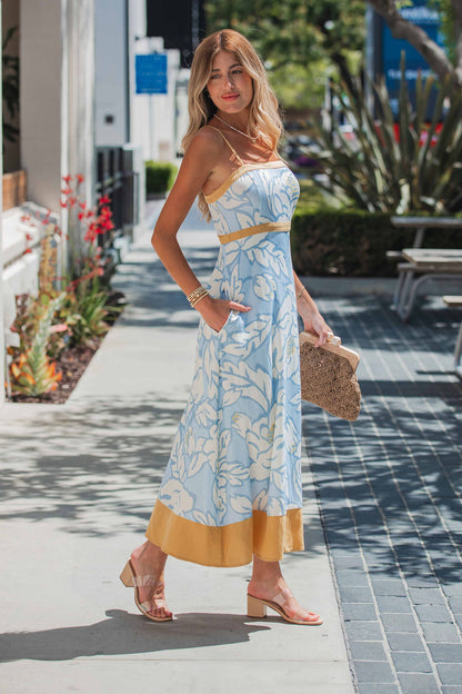 Woman in the Langford Blue Print Maxi Dress, holding a woven clutch—perfect for any summer occasion.