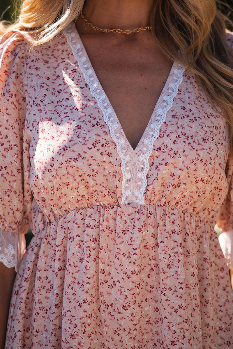 Woman wearing a Beige Floral Lace Tiered Mini Dress with a deep V-neckline and a gold chain necklace.