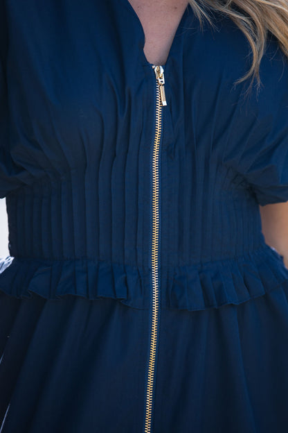 Close-up of the Navy Smocked Zip Midi Dress with gold zipper, pleated waist, and ruffled trim, worn by a blonde model.