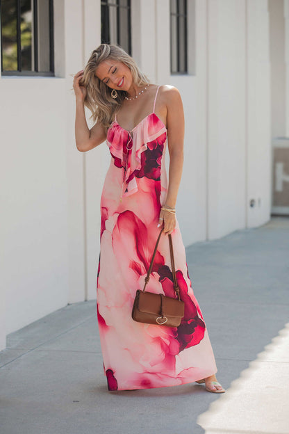 Smiling woman in a Steve Madden Maxinia Coral Print Maxi Dress holds a brown purse, standing by a white building with large windows.