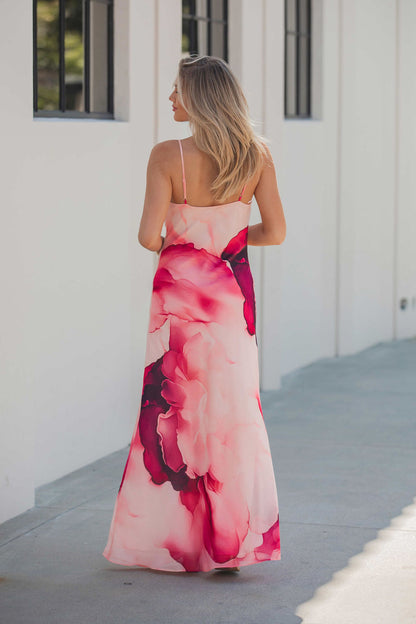 A woman in a Steve Madden Maxinia Coral Print Maxi Dress stands outside by a white building with tall windows.