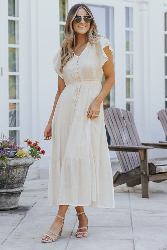 Woman in a Celine Crochet Lace Tiered Boho Midi Dress with sunglasses and sandals, standing near wooden chairs and blooming flowers.
