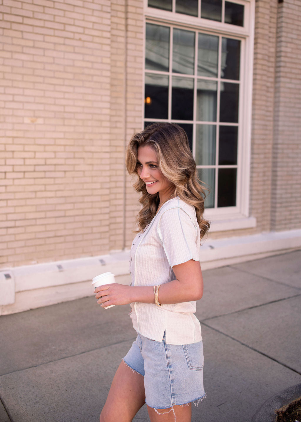 Smiling woman in a Natural Contrast Trim Button Up Top walks outside holding a coffee cup.