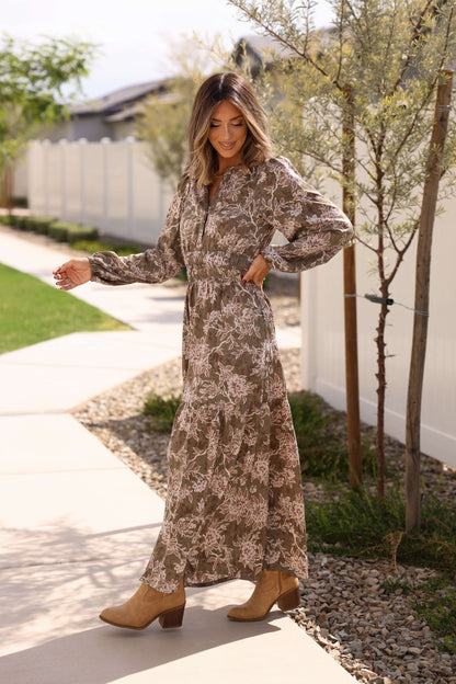 Woman outdoors in a Golden Grove Olive Print Tiered Maxi Dress and tan ankle boots, smiling and looking down while walking.