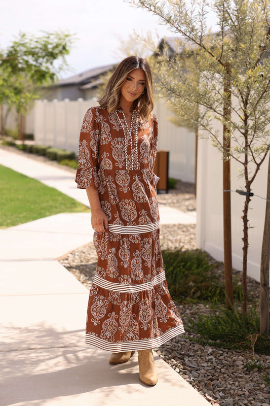 Woman wearing the Harvest Brown Contrast Print Tiered Maxi Dress smiles at the camera on a tree-lined sidewalk.