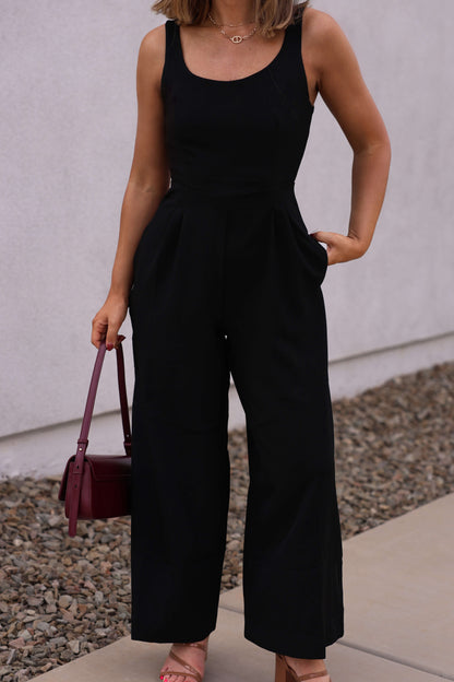 Woman wearing the Hunter and Brown Black Pleated Jumpsuit, holding a burgundy handbag on a rocky sidewalk.