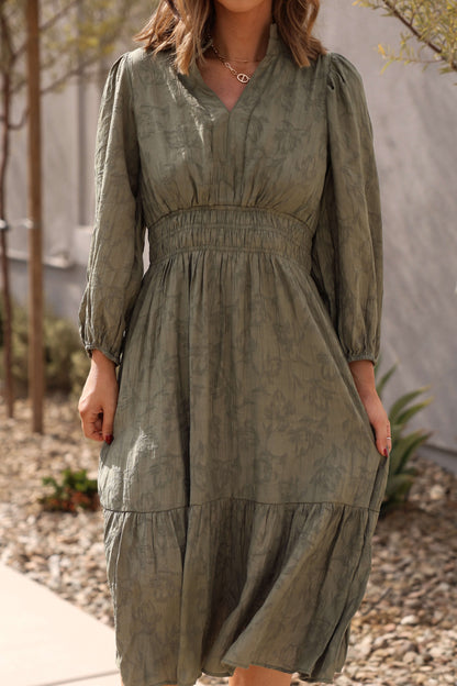 Woman in the Earthy Olive Floral Print Midi Dress stands outdoors on a stone path with lush plants behind her.