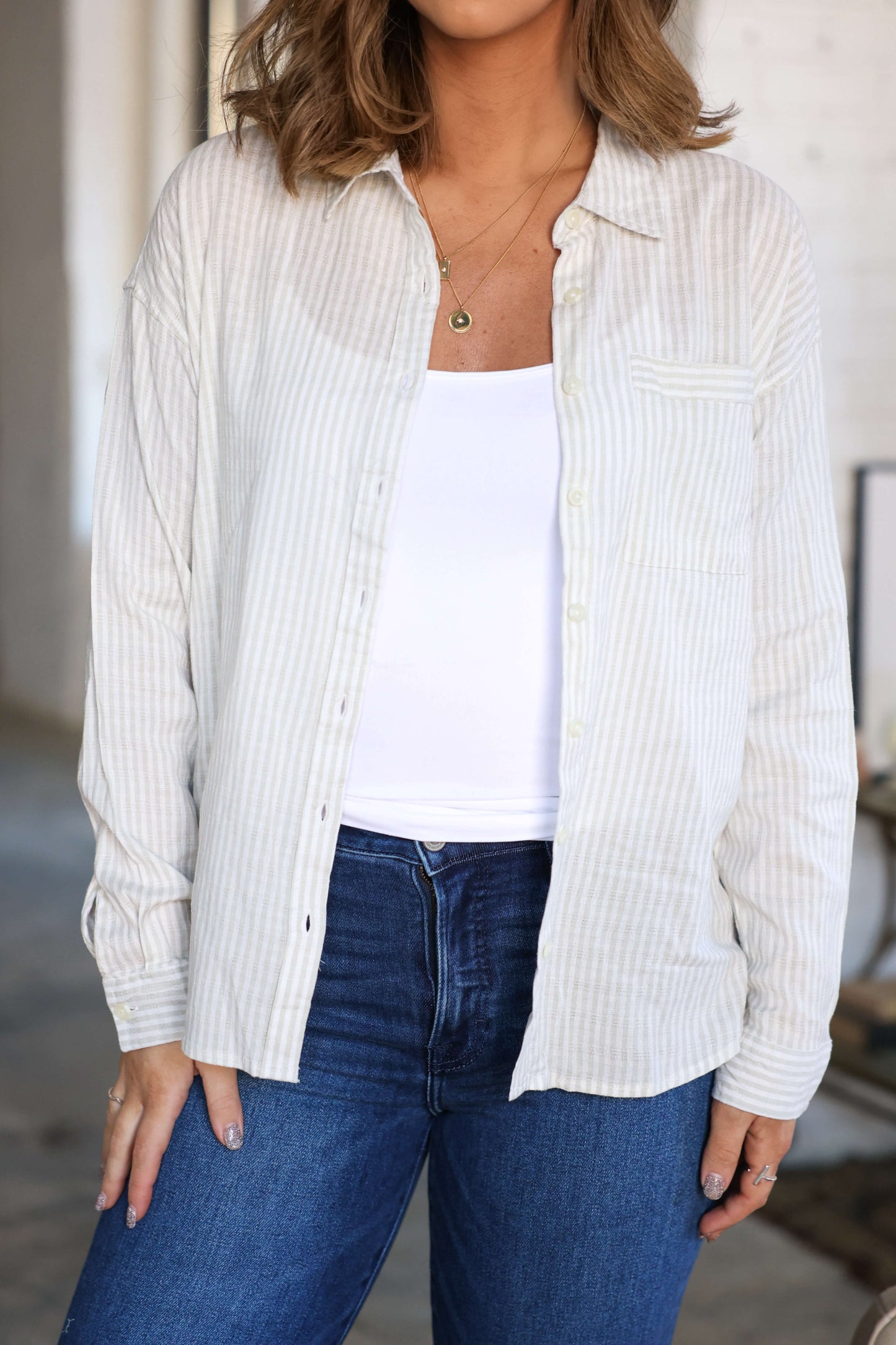 Woman wears the Thread and Supply Edison Tan Striped Shirt | Pre Order over a white top and blue jeans, standing indoors relaxed.