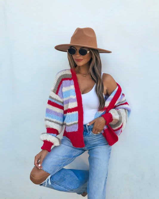 A woman wearing a Striped Cardigan - Fuchsia, white tank top, blue jeans, sunglasses, and a tan hat.