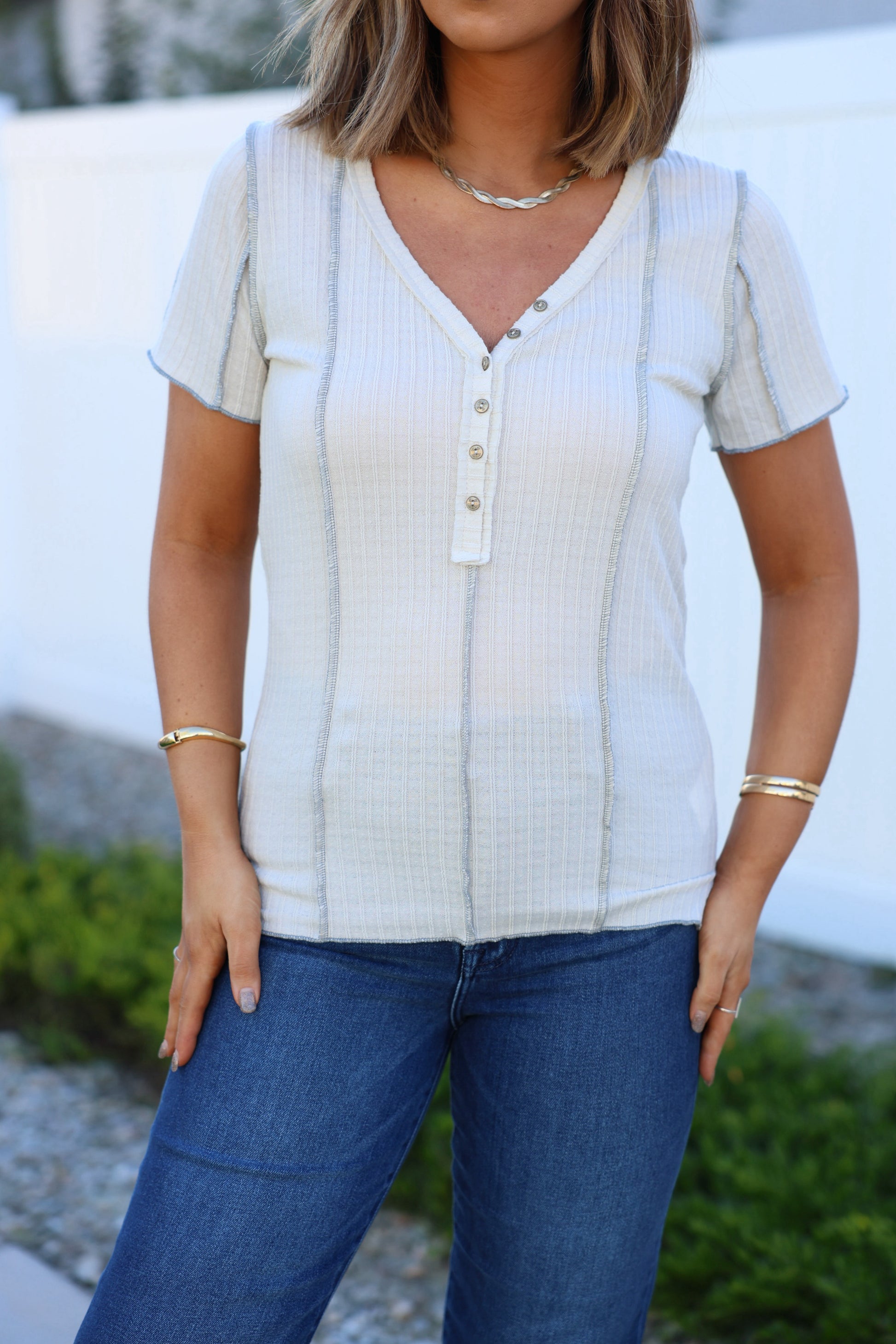 Woman wearing the Natural Contrast Trim Button Up Top and blue jeans, standing outdoors by greenery and a white fence.