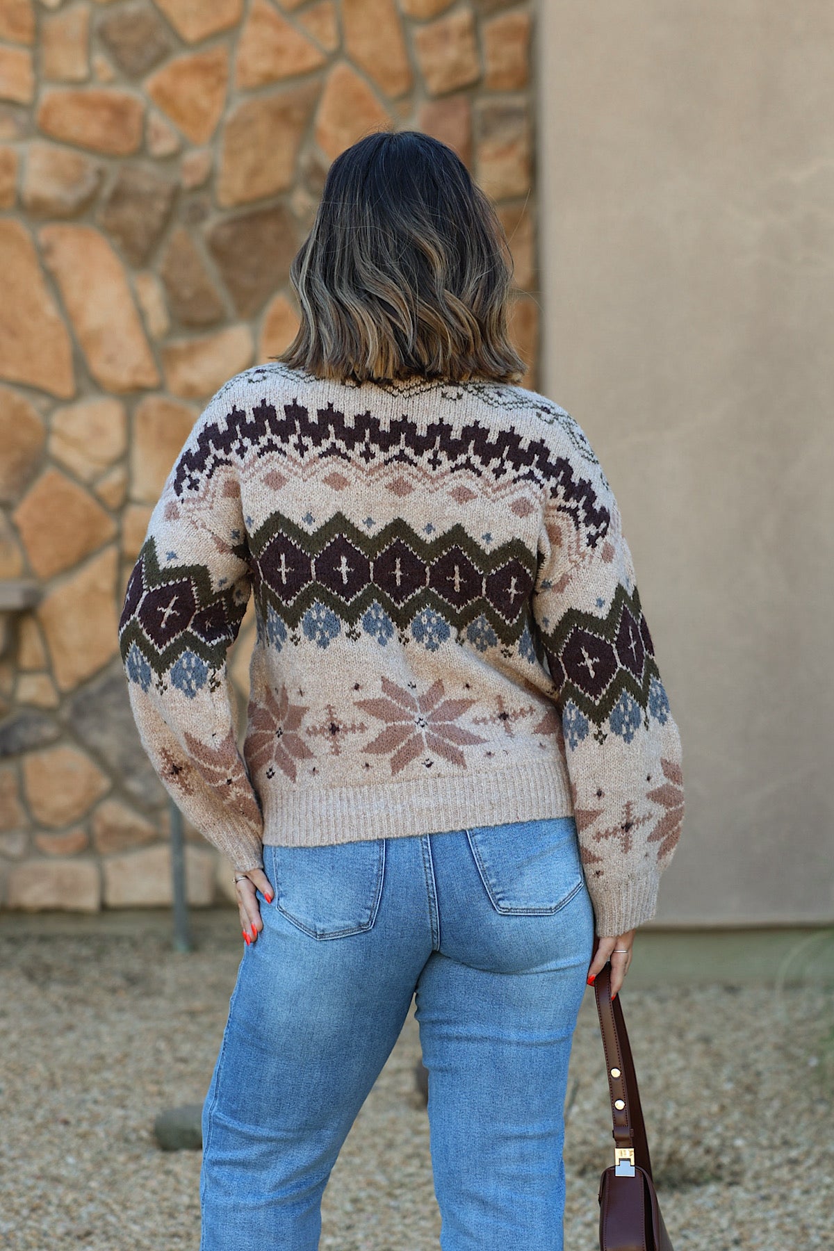 A person seen from behind wears a Light Khaki Fair Isle sweater with dark brown, green, and blue geometric patterns paired with blue jeans.