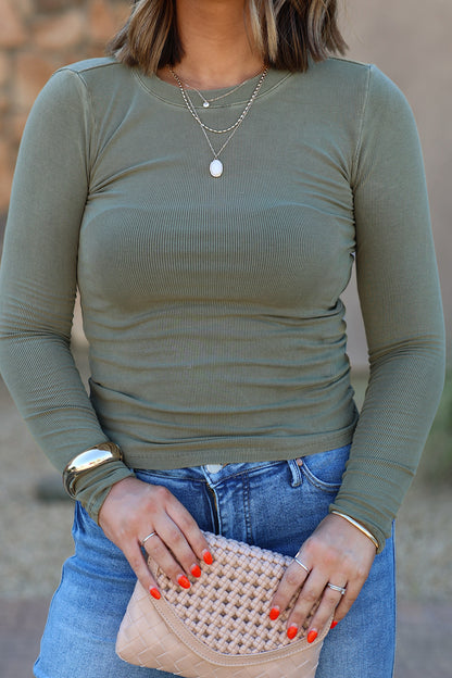 Woman in Ultra Soft Basic Ribbed Top - Dark Olive & jeans holds a beige clutch, with orange nails and layered necklaces.
