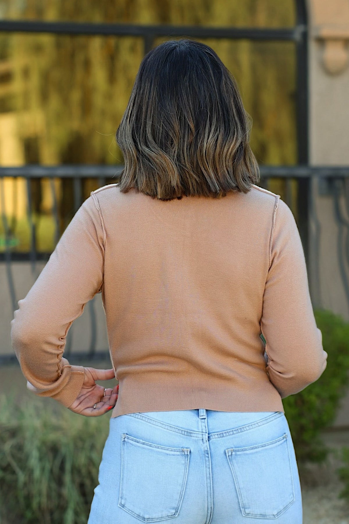 A person from behind wearing a Taupe Color Block Button Down Sweater and light-wash jeans.