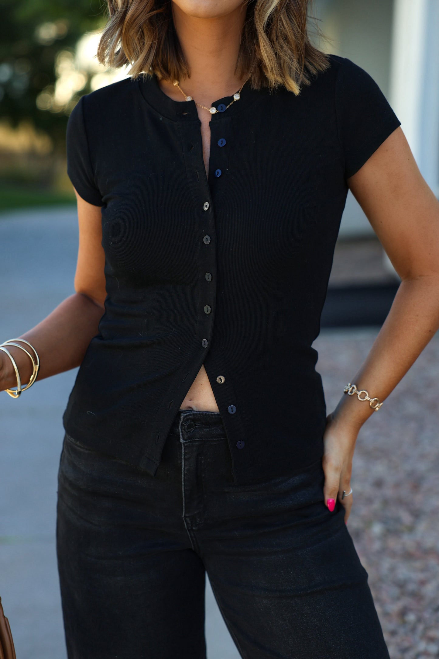 A woman outdoors in a Black Button Front Short Sleeve Sweater and black jeans, accessorized with bracelets.