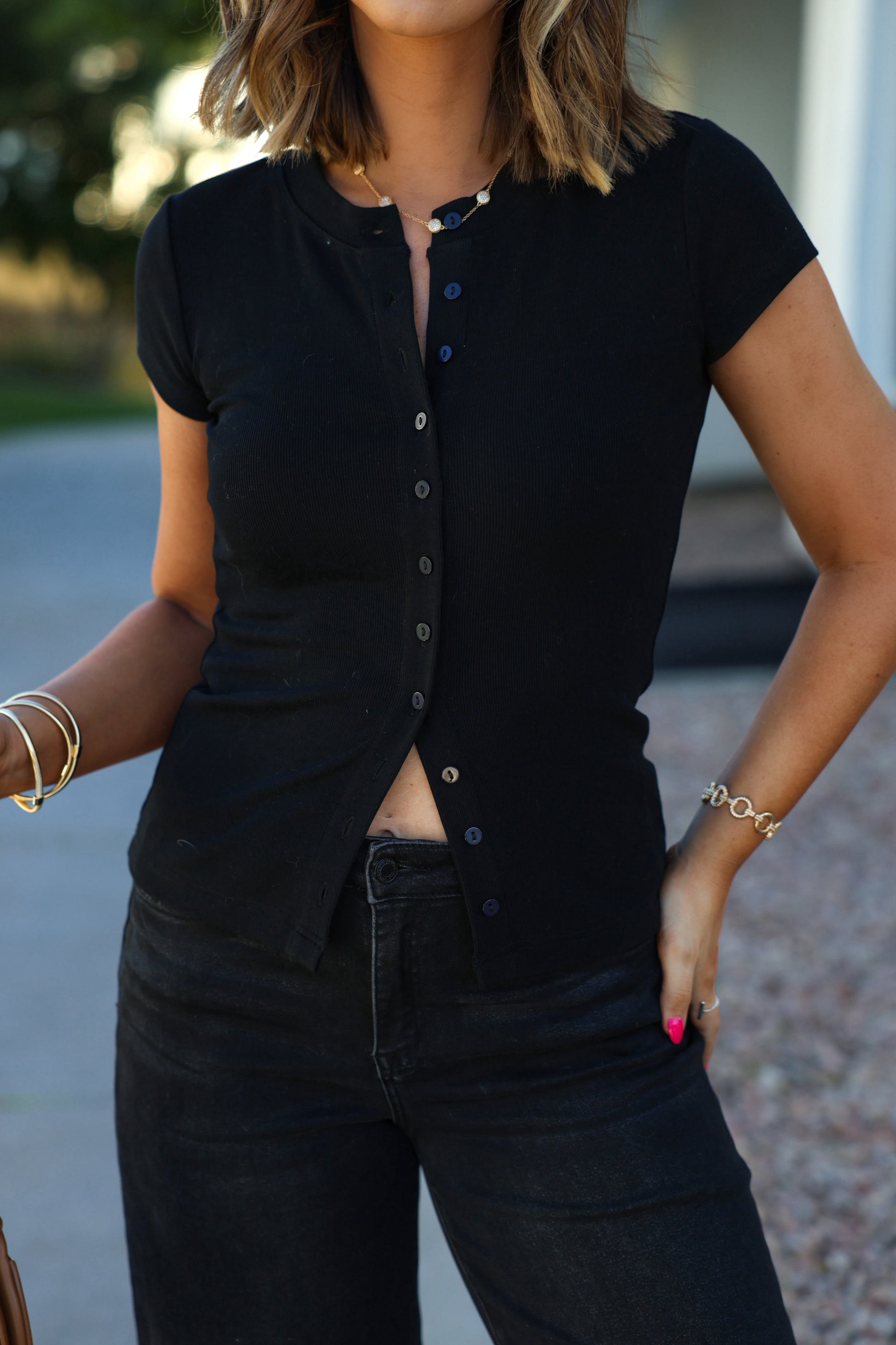 A woman outdoors in a Black Button Front Short Sleeve Sweater and black jeans, accessorized with bracelets.