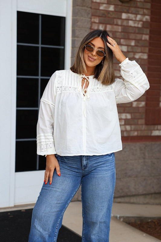 A woman wears an Off White Crochet Long Sleeve blouse with a lace-up neckline and blue jeans.