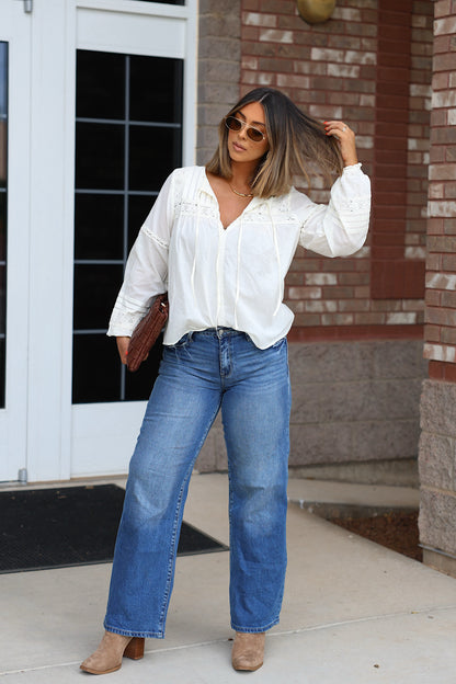 A woman wearing a white long-sleeve blouse, Petra Low Rise Ultra Loose Jeans, and tan ankle boots.