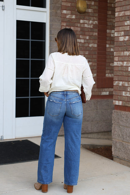 Person seen from behind wearing a white long-sleeved blouse, Petra Low Rise Ultra Loose Jeans, and tan heeled boots.