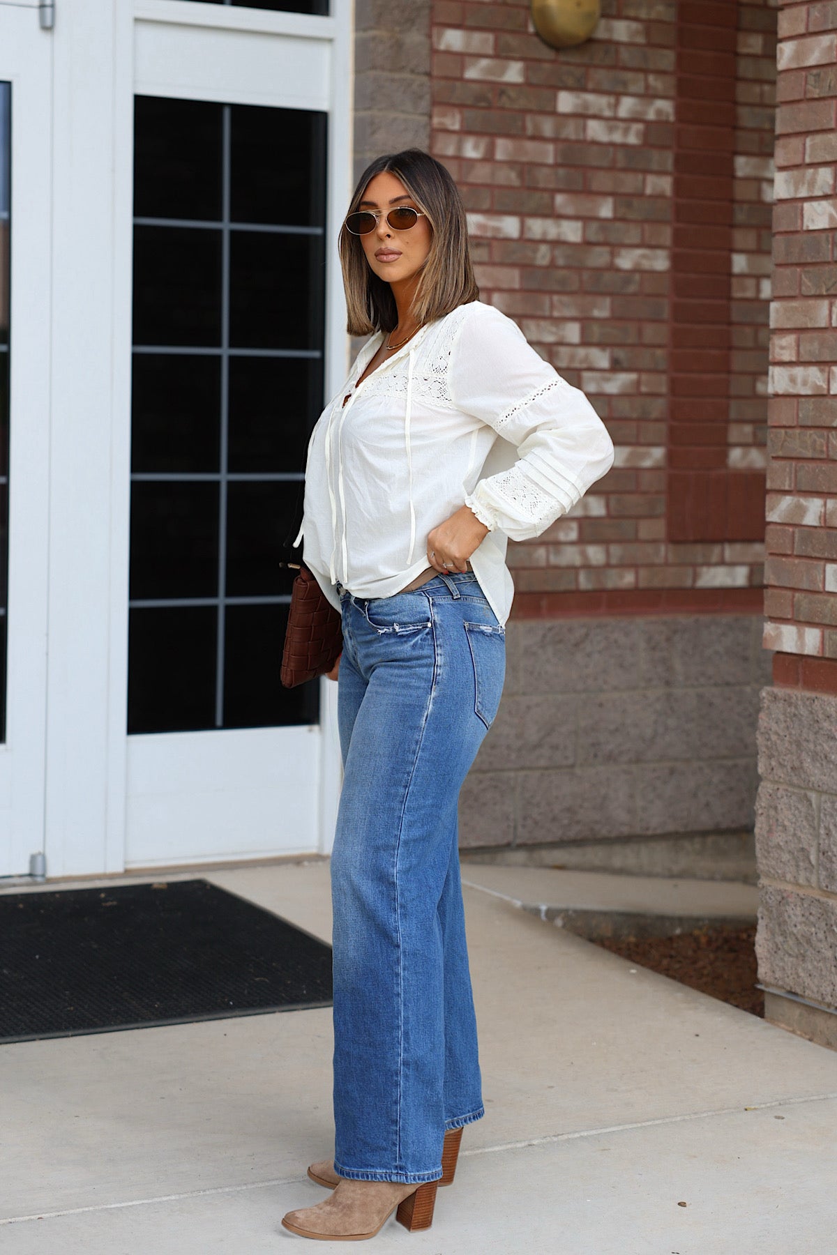 Woman wearing a white long-sleeve peasant blouse, Petra Low Rise Ultra Loose Jeans, and tan heeled boots.