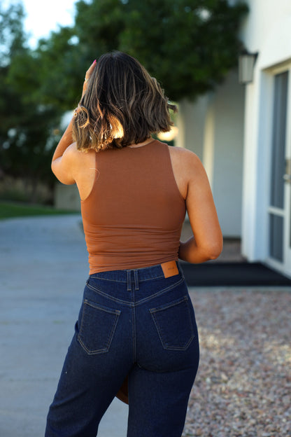 A woman in a Basic Caramel Double Lined Tank Top and blue jeans stands outside, facing away from the camera.