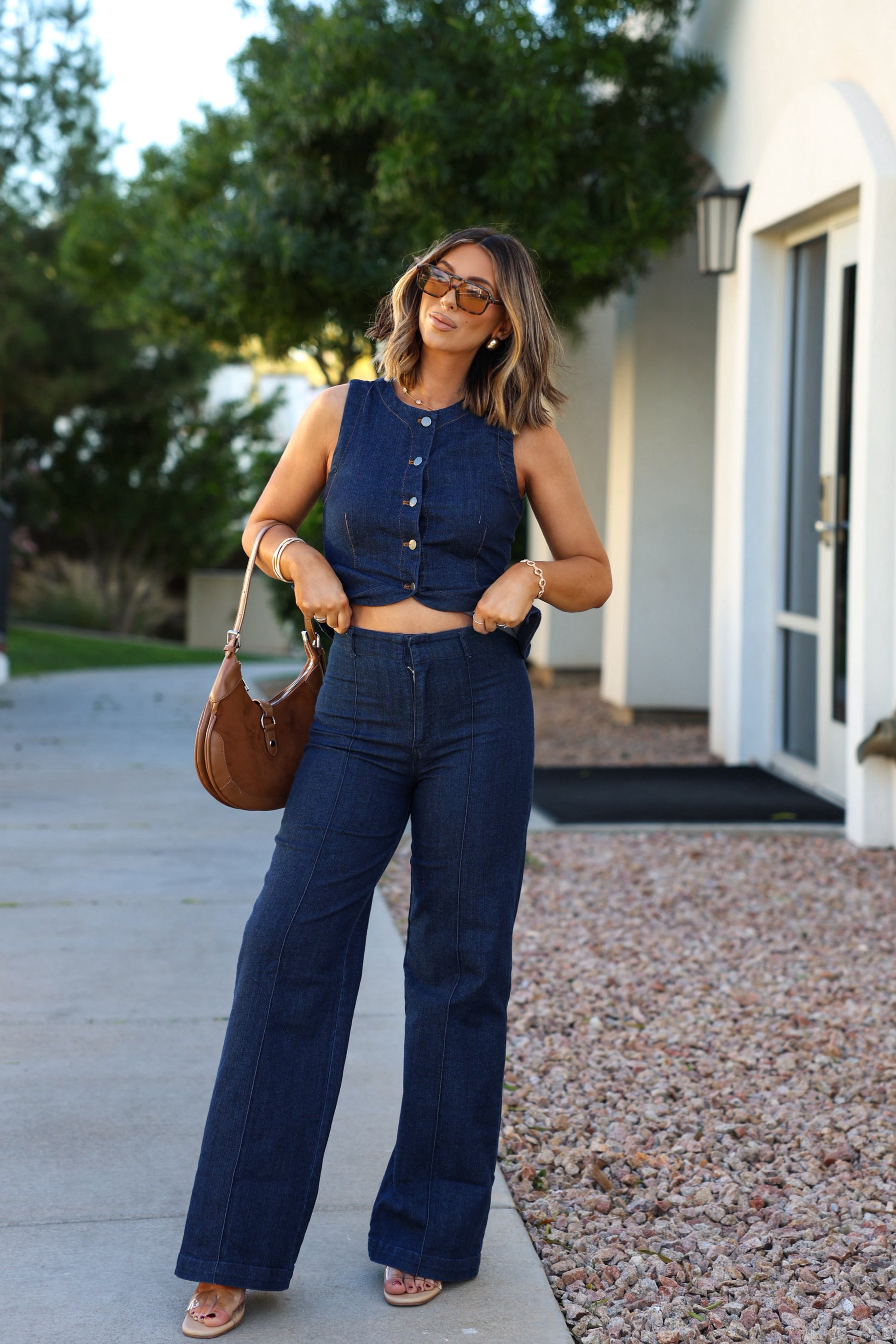 A woman wears a Dark Denim Button Down Vest and wide-leg jeans outside, holding a brown handbag and smiling.